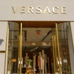 Luxury Versace store entrance with gold signage, glass doors, and high-end fashion displays inside.