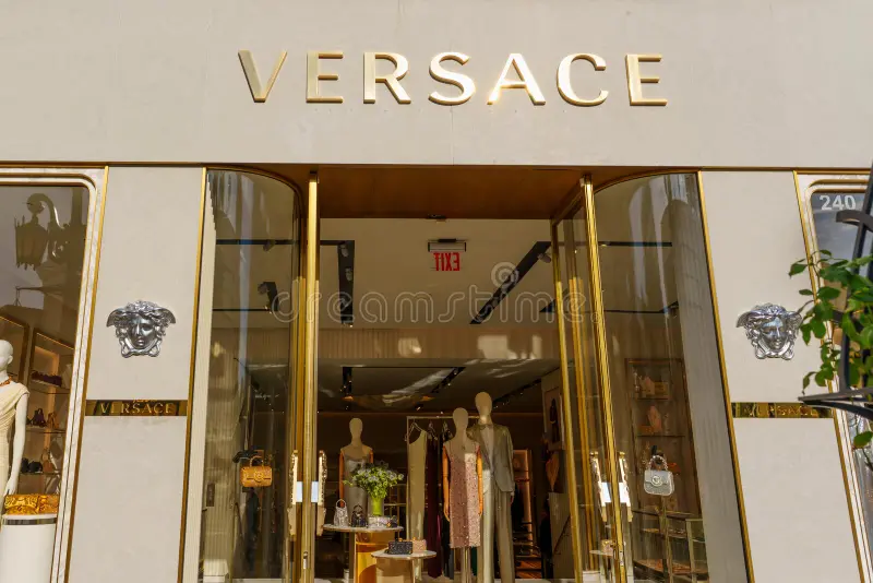 Luxury Versace store entrance with gold signage, glass doors, and high-end fashion displays inside.